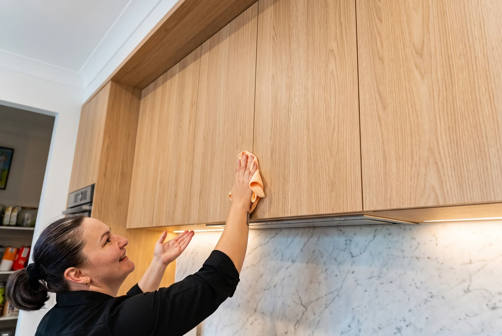 Wiping down oak kitchen cupboards above a marble splashback